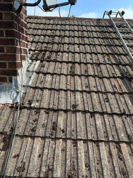 Moss across the tiles and patched flashing at the chimney abutment